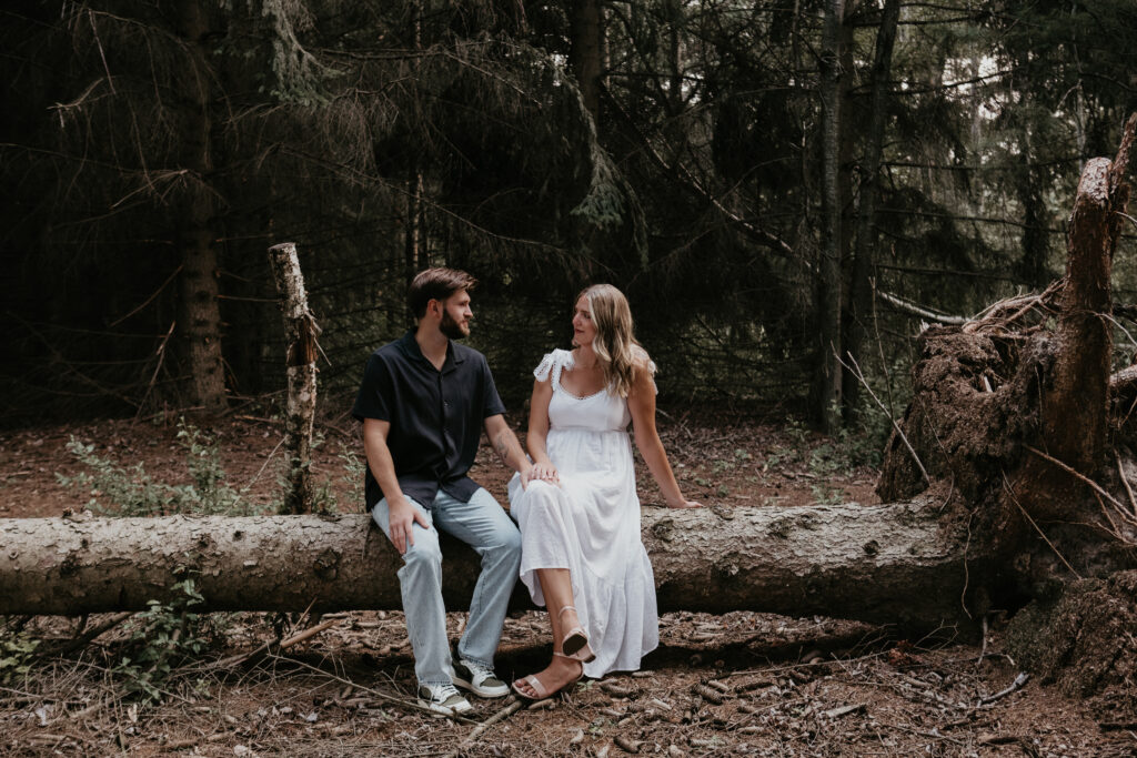 Couple sitting together on a fallen tree during their engagement session in the woods of Michigan