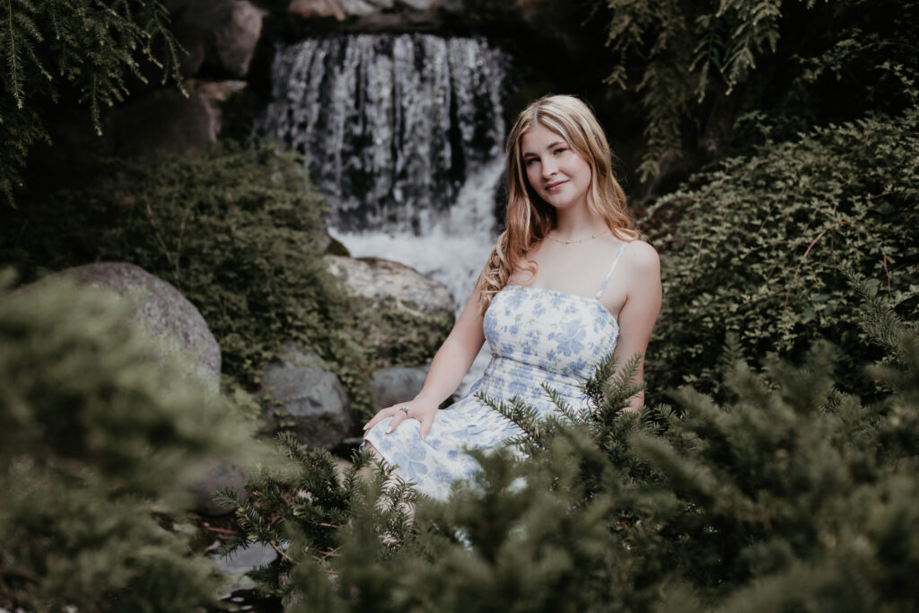 Senior girl sitting in front of a waterfall at Dow Gardens during her portrait session with Arielle Roth Photography in Michigan
