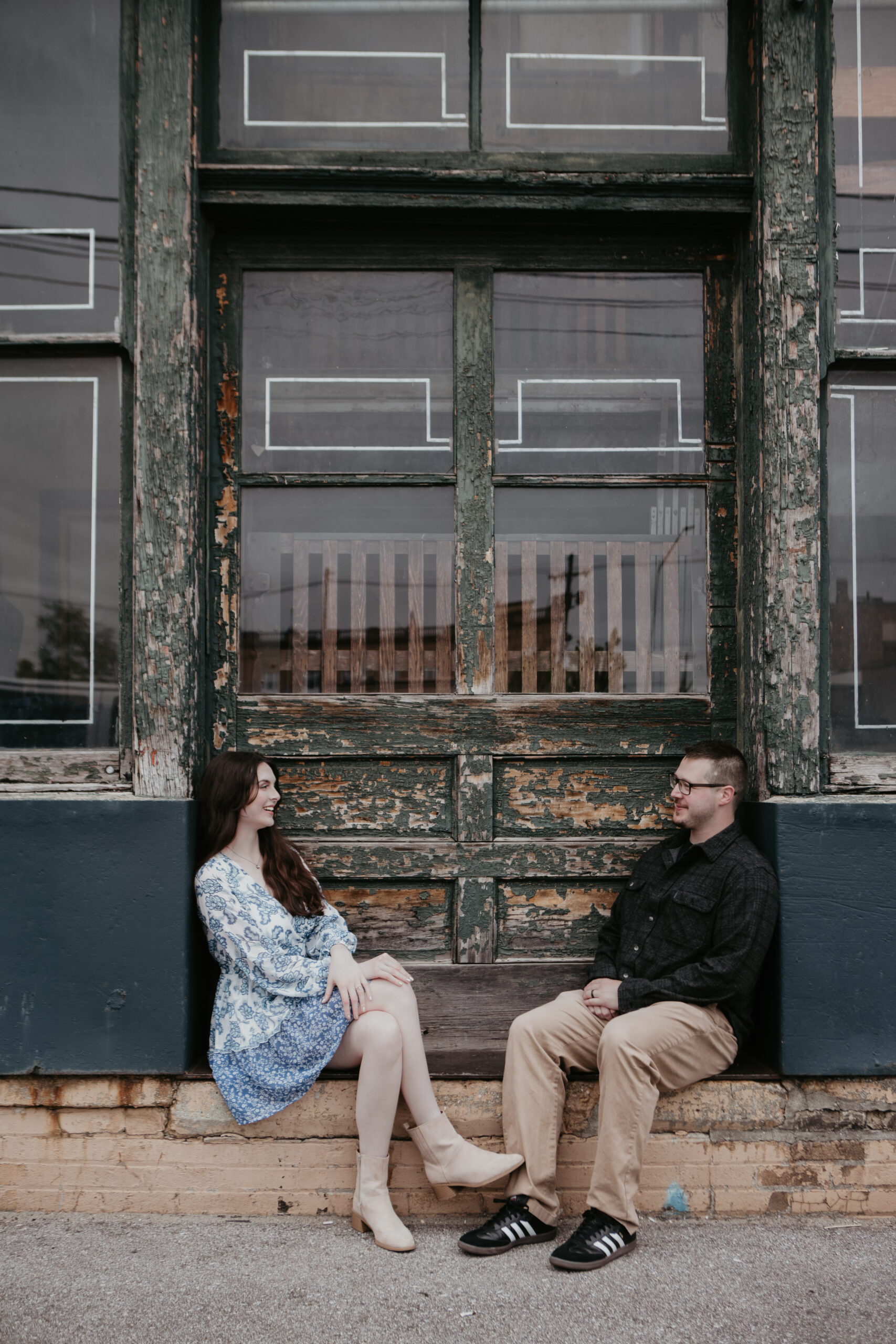Lansing couple during their Downtown Bay City engagement session sitting together in front of a rustic, weathered building.