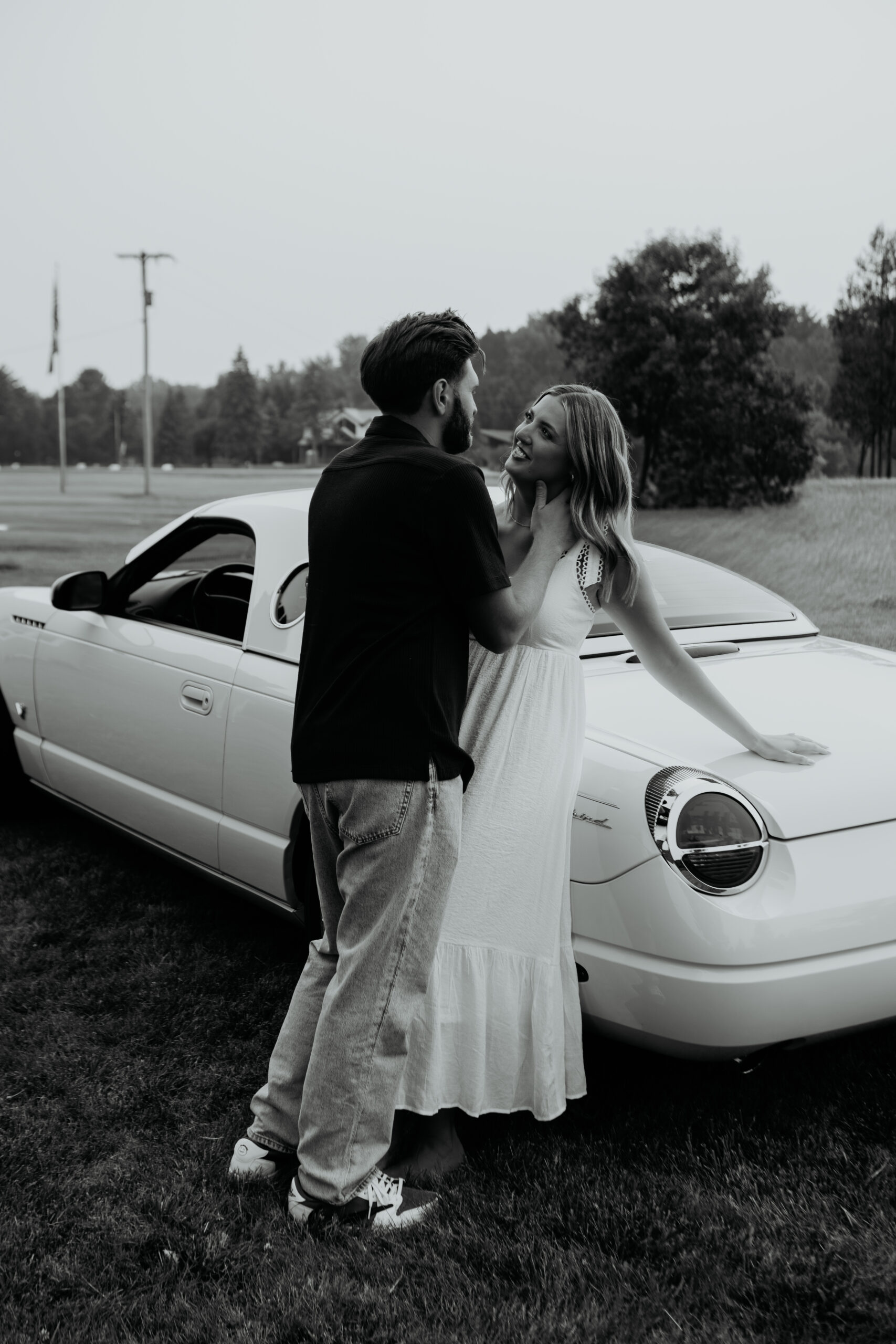 Engaged couple laughing together by vintage white car during Michigan engagement photos