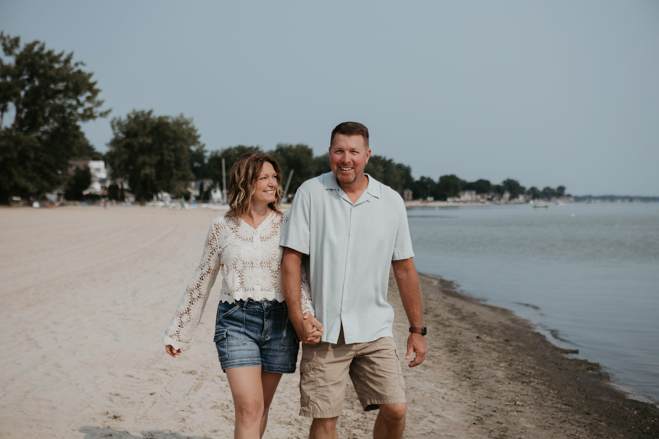 Couple walking hand in hand along the shoreline at Bay City State Park during their summer Michigan photo session