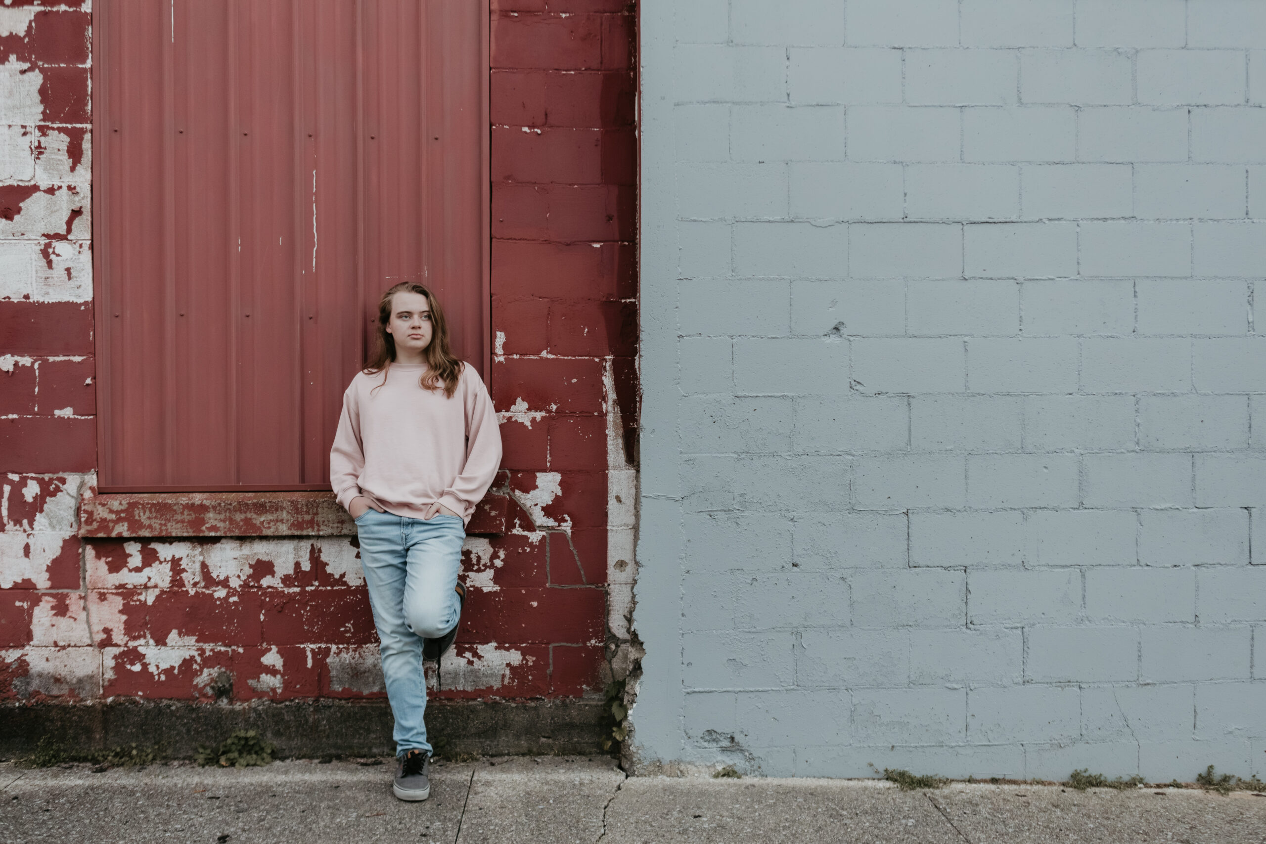 Senior photo of Ethan leaning against a rustic red and gray wall in downtown Cass City, Michigan, captured by Arielle Roth Photography.