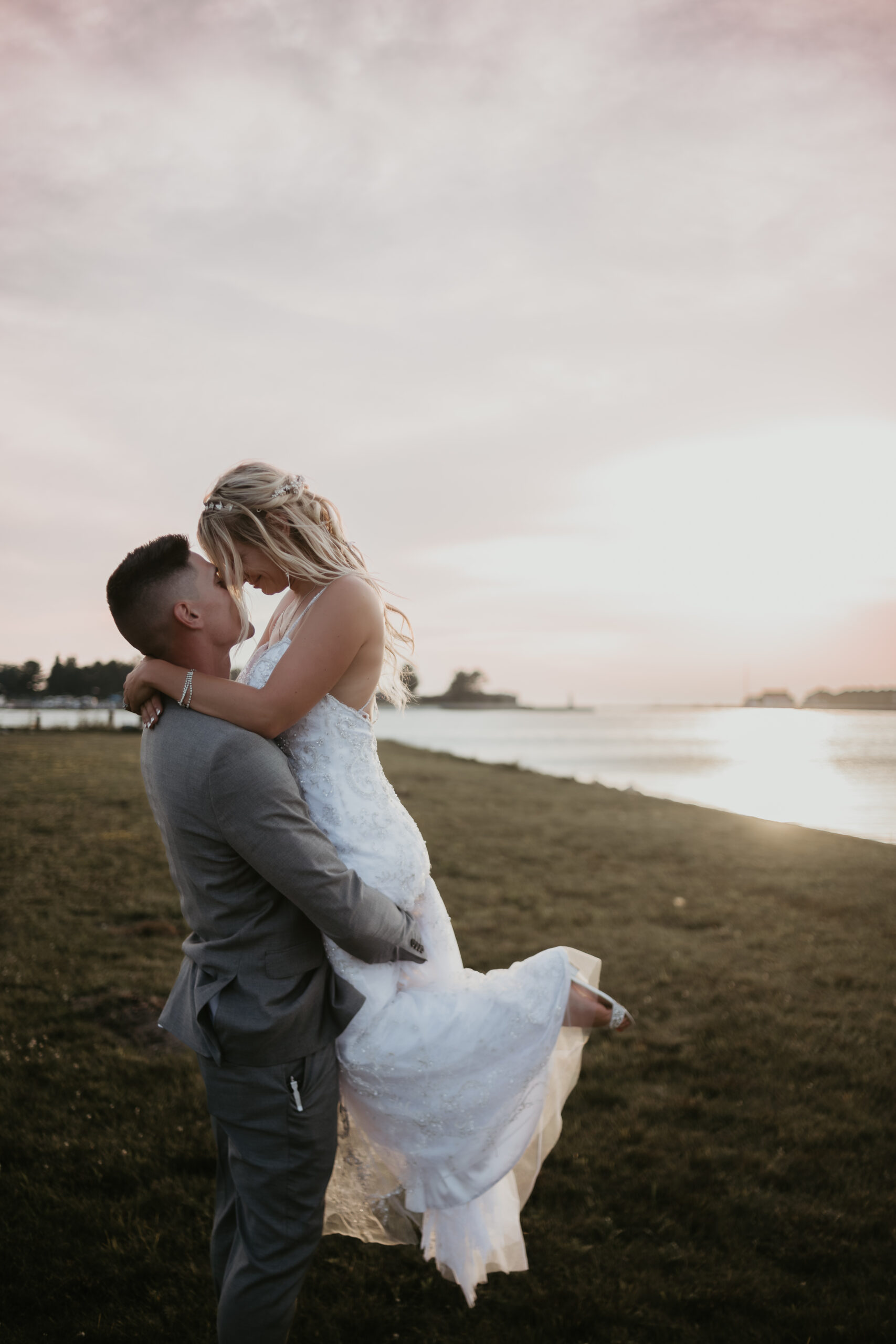 Groom lifts bride in his arms at sunset by the waterfront at The Lake House in Ludington, Michigan.