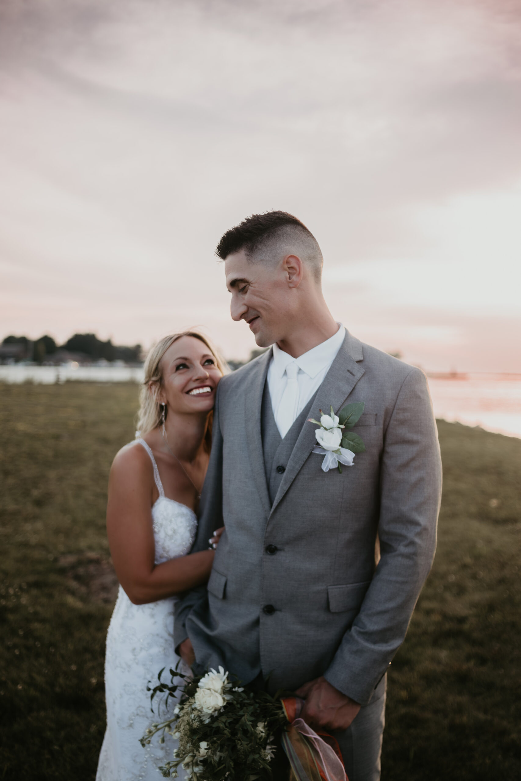 Bride smiles up at her groom during sunset wedding portraits at The Lake House in Ludington, Michigan.