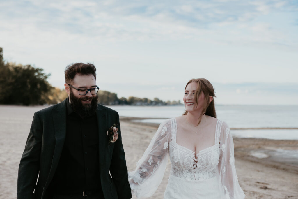 Christie and Jordan walk hand in hand along the shoreline at Bay City State Park during their elopement, captured by Arielle Roth Photography in Michigan.