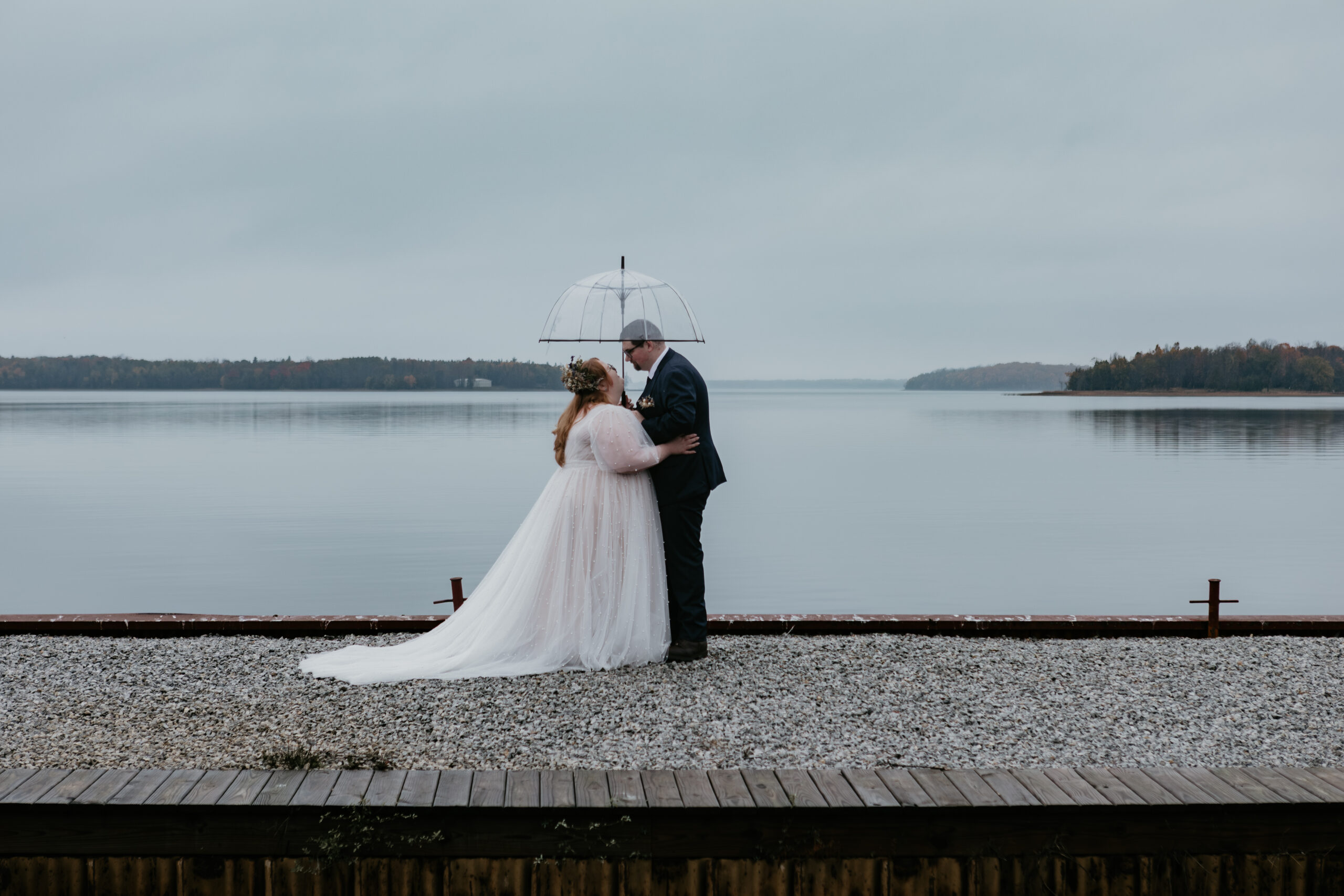 Bride and groom sharing a kiss under a clear umbrella by the water at Drummond Island Resort in Michigan, photographed by Arielle Roth Photography.