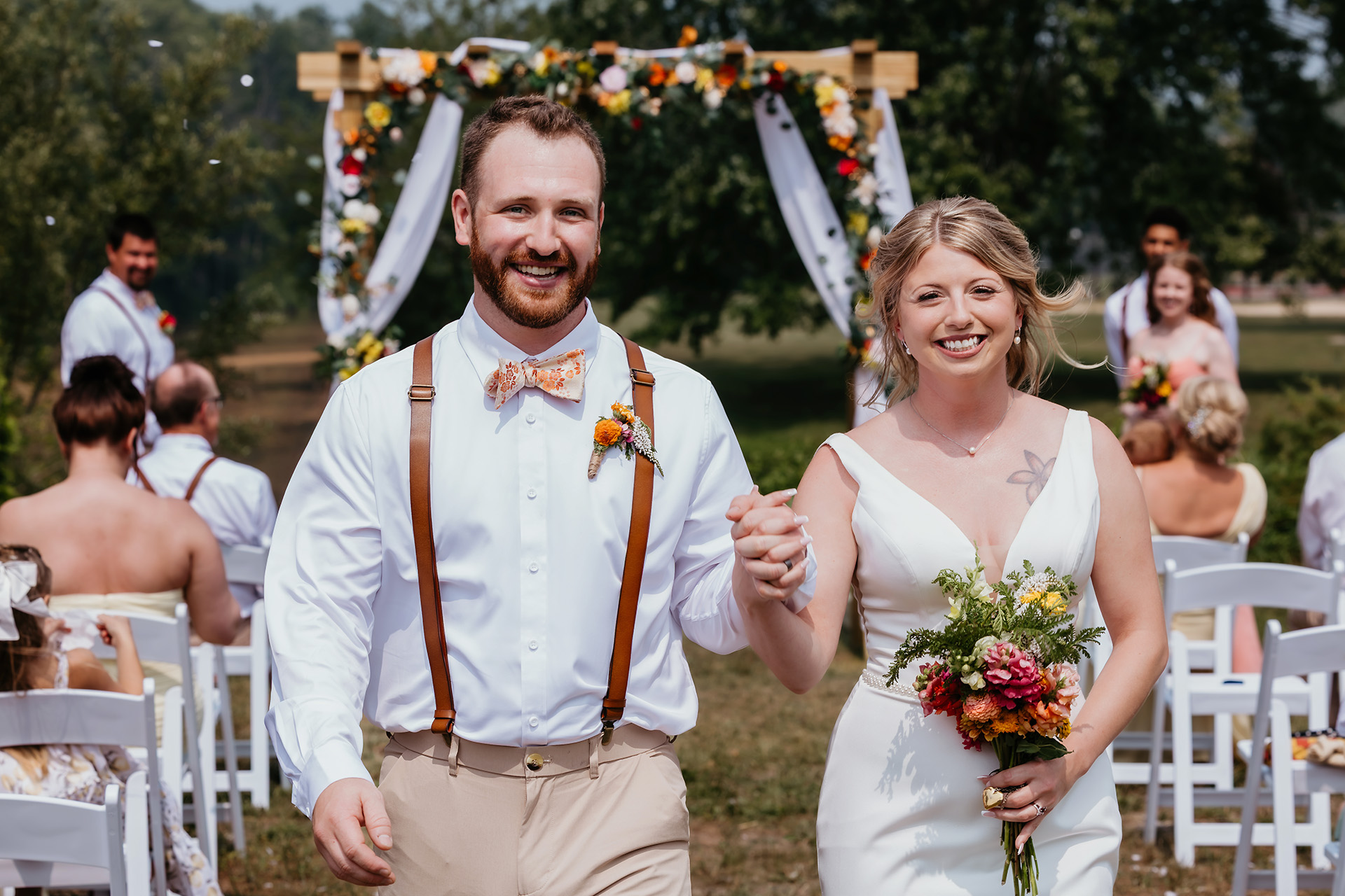 Newlyweds Erica and Tyler smiling and holding hands as they walk back down the aisle after their outdoor wedding ceremony at Rivermill Wedding Venue in Au Gres, Michigan.